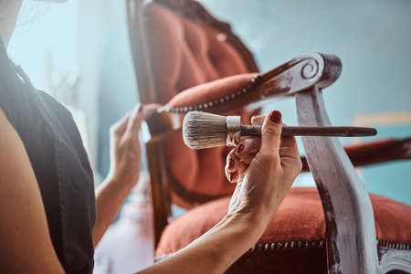 Female artist painting vintage chair in white color with paintbrush in workshop.の写真素材