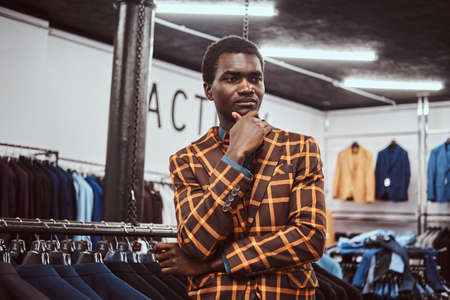 Elegantly dressed African man posing with hand on chin while standing in a classic menswear store.の写真素材