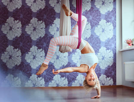 Young woman doing aerial yoga practice in purple hammock in fitness club.の写真素材