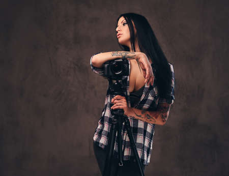 Seductive tattooed girl wearing an unbuttoned checked shirt girl posing with a camera.