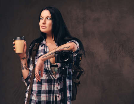 Tattooed girl holding a takeaway coffee while leaning on a camera in a studio.の写真素材