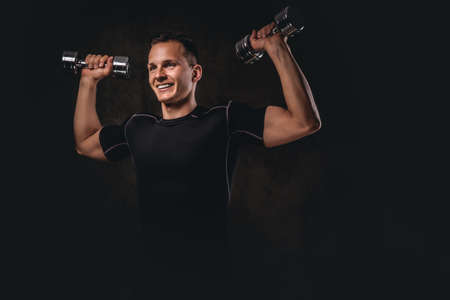 A young bodybuilder wearing sportswear doing exercise with dumbbells on dark background.の写真素材