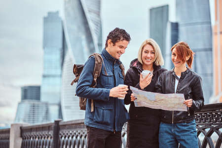 Group of happy tourists searching place on the map in front of skyscrapersの写真素材