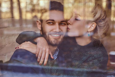 Beautiful girl sitting on her boyfriends lap on the cafe behind the window.の写真素材