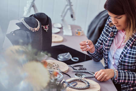 Elegantly dressed woman makes handmade necklaces, working with needles and thread in workshop.の写真素材