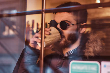 A handsome young stylish man drinking coffee in the cafe behind the window.の写真素材