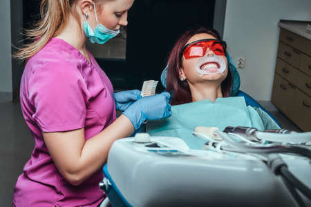 A woman dentist checks the level of teeth whitening with a dentists color in the dentist office.の写真素材
