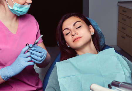 Woman patient sitting in a dentist chair while her doctor preparing for syringe injection.