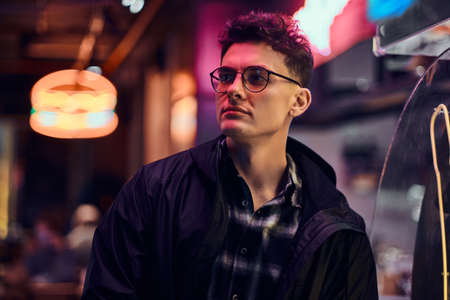 A handsome young man standing at night in the street. Illuminated signboards, neon, lights.