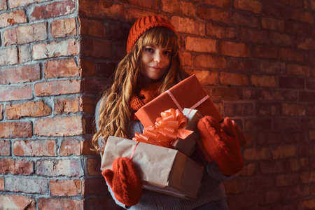 Portrait of a lonely redhead girl wearing a warm sweater and hat holding gift boxes while leaning on...