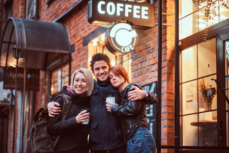 Happy friends standing together in an embrace near a cafe outside.の写真素材