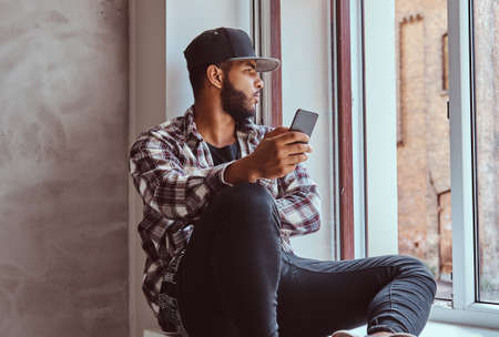 African-American bearded man sitting on a window sill.の写真素材