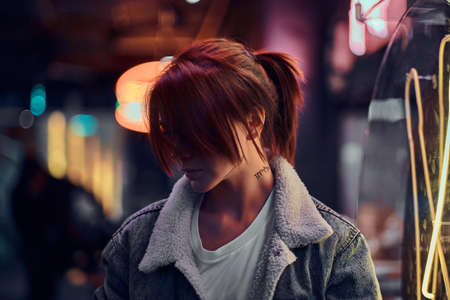 Stylish redhead girl standing in the night on the street. Illuminated signboards, neon, lights.