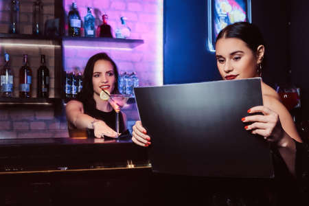 A beautiful girl sitting at the bar counter and reading menu in the nightclubの写真素材