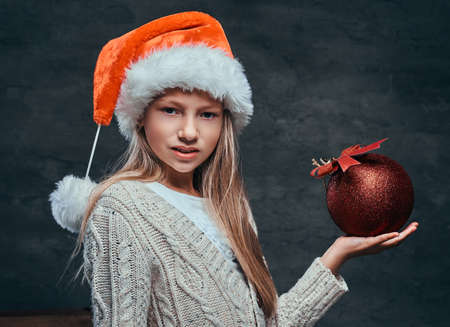 Teen boy wearing Santas hat holding a big Christmas ball on a dark textured background.の写真素材