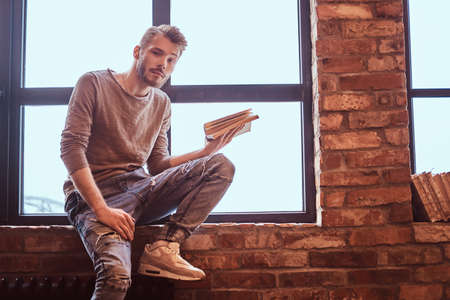 A young handsome student with stylish beard and hair holding a book and looking at cameraの写真素材