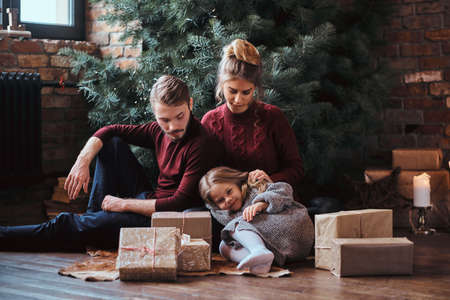 Attractive family sitting together on a floor surrounded by gifts next to the Christmas tree.の写真素材
