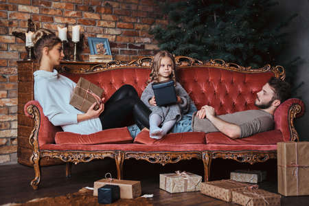 Happiness cute little girl sitting with her parents on a vintage sofa surrounded by gifts.の写真素材