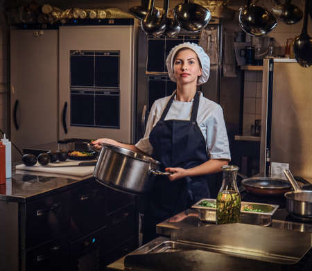Female chef wearing a uniform holding a pan at restaurants kitchen.の写真素材