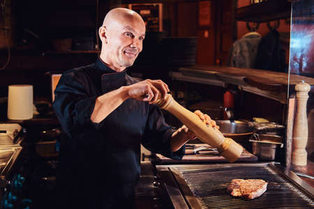 Master chef cooking delicious beef steak on a kitchen in a restaurant, pepper the meat with a pepper...