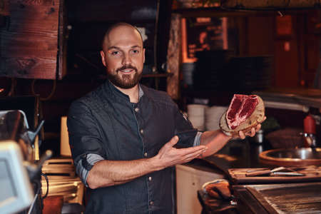 Chef presenting a fresh steak before cooking and looking at a camera in a restaurant kitchen.の写真素材