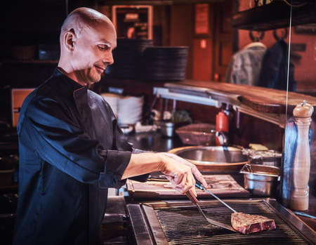 Focused master chef wearing uniform cooking delicious beef steak on a kitchen in a restaurant.の写真素材