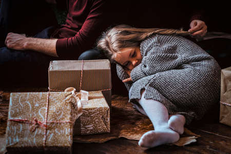 A cute little girl wearing a warm sweater sleeping while lying on a rug next to her parents, surrounded by gifts.の写真素材