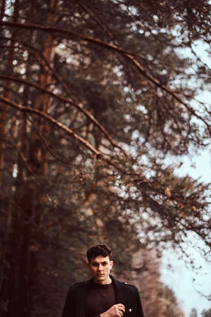 Young man with coat covering his shoulders in the autumn forest.の写真素材