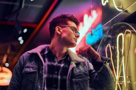 A pensive young man leaning on an illuminated signboard in the street at night.の写真素材