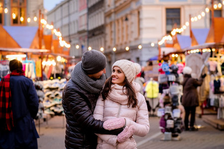 A young romantic couple wearing winter clothes hugging while standing in evening street with Christmas fairの写真素材