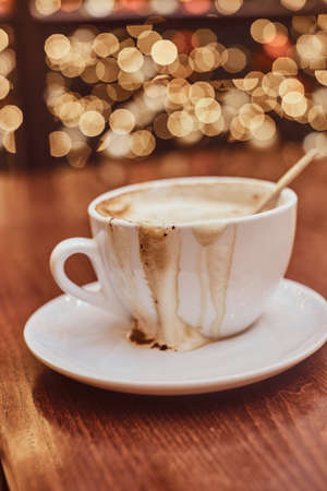 Cup with spilled coffee on the wooden table in a coffee shop, blur background with bokeh effectの写真素材