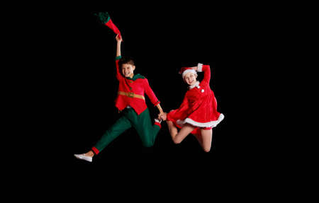 Christmas time, childhood, fairy tale. A young girl wearing a Santas costume and boy wearing elf costume flying togetherの写真素材