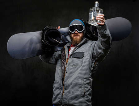 Cheerful redhead man wearing a full equipment for extreme snowboarding holding a snowboard on his...