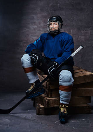 Bearded hockey player wearing full sports equipment holding a hockey stick while sitting on wooden pallets.の写真素材