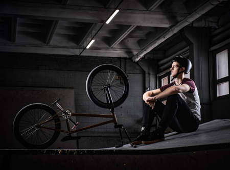 Young Bmx rider relaxing after practicing tricks with his bike in a skatepark indoorsの写真素材