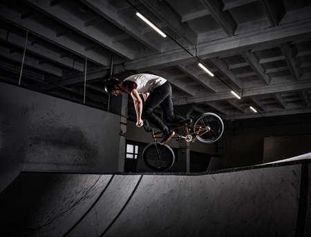 Professional BMX rider in protective helmet performing tricks in skatepark indoorsの写真素材