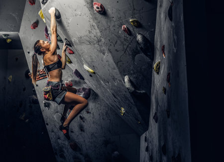A young woman wearing sportswear practicing rock-climbing on a wall indoorsの写真素材