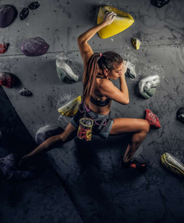 A young woman wearing sportswear practicing rock-climbing on a wall indoorsの写真素材