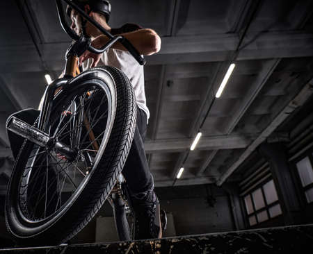 Professional BMX rider in protective helmet sitting on his bicycle in a skatepark indoorsの写真素材