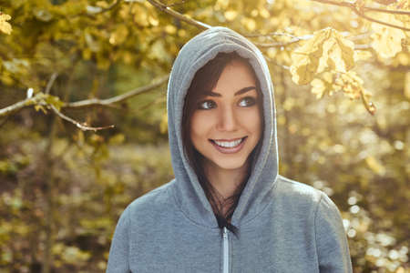 Close-up portrait of a smiling beautiful girl wearing a gray hoodie in the autumn parkの写真素材