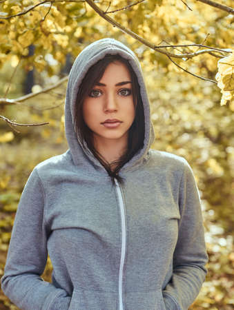 Close-up portrait of a charming girl wearing a gray hoodie in the autumn parkの写真素材