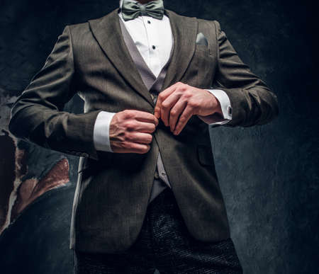 Cropped image of a stylish young man buttoning his elegant jacket against a dark textured wallの写真素材