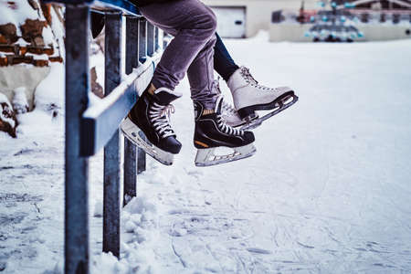 Couple wearing ice skates sitting on a guardrail. Dating in an ice rink.