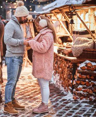 An attractive couple in love. A handsome man and his beautiful girlfriend holding hands, enjoying spending time together, standing at the winter fair at a Christmas timeの写真素材