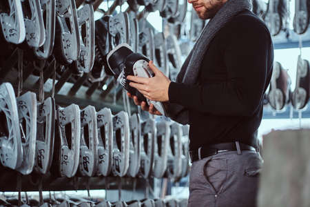 A young guy wearing warm clothes standing next to a rack and choosing a pair of skates in a locker...
