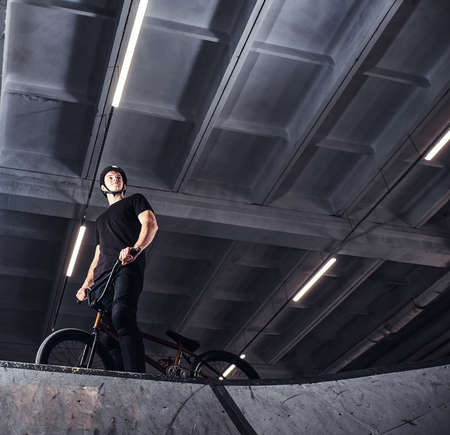 Professional BMX rider in protective helmet getting ready to jump in a skatepark indoorsの写真素材