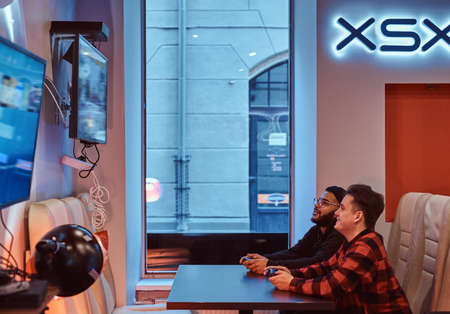 Two multiracial friends, enjoying spending time, playing in a multiplayer video game on a game...