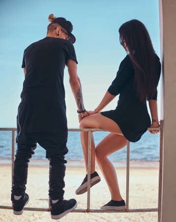 Back view of a young stylish couple in love on vacation at the seaside, enjoy spending time...