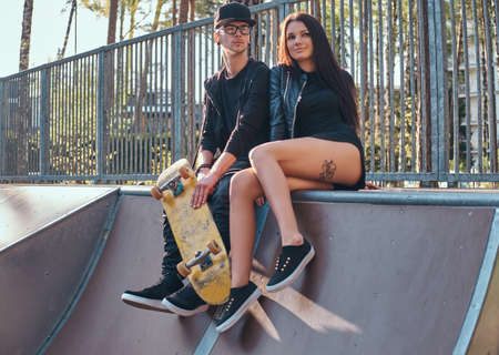 Young couple in love sitting together on a ramp in the skate park at the summertime