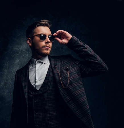 A confident elegantly dressed young man in sunglasses posing against a dark textured wallの写真素材